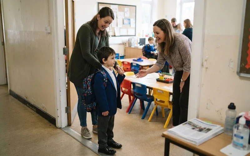 A young child wearing a school backpack walking hand in hand with a parent toward a primary school entrance