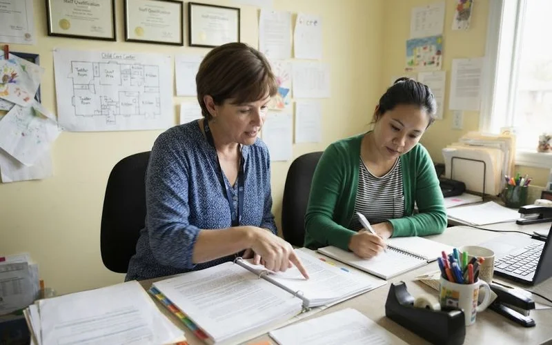A parent talking with a centre director in an office while reviewing compliance documents and certificates