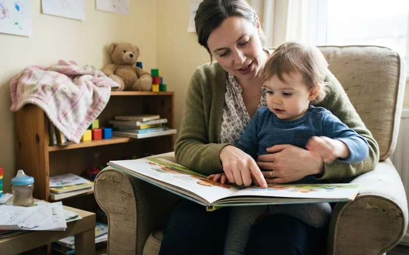 A parent crouching down to say goodbye to a toddler at a nursery room entrance while an educator waits nearby